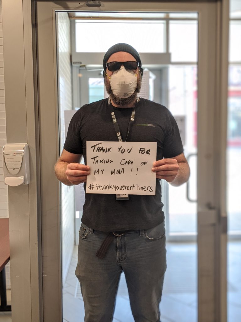 Young man wearing a mask holds a sign says "thank you for taking care of my mum".