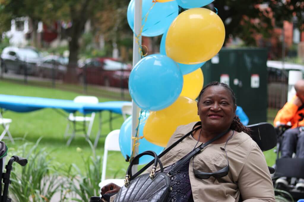 Bellwoods client in a wheelchair outdoors beside blue and yellow balloons