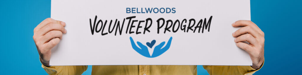 Hands holding paper sign with "Bellwoods Volunteer Program" printed on it